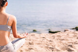 Fototapeta Las - rear view of a young woman doing meditation at beach sitting with legs crossed, concept of mental relaxation and healthy lifestyle
