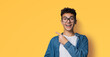 Excited happy black curly haired man in braces, open mouth, wear glasses denim shirt advertise show point area for sales slogan text, isolated yellow background. Dental care ophthalmology ad.