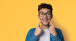 Dental dent care ad concept image - black сurly haired funny young man wear metal braces, eye glasses, show point white teeth smile. Isolated against yellow wall background. Positive optimistic.