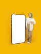 Full body muslim woman, studio shot portrait of full body muslim woman in hijab pointing big huge empty touch screen mobile phone mock up. Online smartphone application advertisement concept.