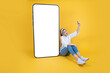 Full body woman sit floor leaning empty blank white screen big huge mobile phone mock up taking selfie photo. 20s young caucasian blonde girl posing over yellow studio background. Copy space.
