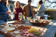 A cozy outdoor gathering features friends enjoying drinks and a lavish charcuterie board filled with cheeses, fruits, and meats under soft sunlight.