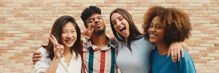 Wall Mural - Happy, lovely multiethnic young people posing for the camera on summer day outdoors, Panorama. Group of friends hugging tightly smiling at camera while standing on brick wall background