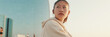 © Andrii Nekrasov - Asian girl in sportswear is resting in the training field, standing on modern buildings background at morning time, Panorama