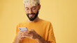 Smiling guy with glasses, dressed in yellow T-shirt, writing sms on mobile phone, isolated on yellow background in studio