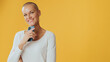 Smiling young hairless woman with mobile phone in her hands looking at camera, advertising space, isolated on yellow background in studio