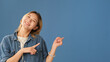 Young woman dressed in denim shirt shows finger at mockup space isolated on blue background in studio