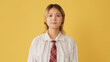 Young woman dressed in shirt and tie listens carefully and disagrees isolated on yellow background in studio