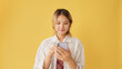 Smiling young woman wearing shirt and tie using mobile phone isolated on yellow background in studio