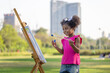 Kid girl painting on the canvas in the park. Happy child girl drawing a picture outdoors