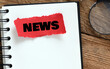NEWS word written on a red piece of paper placed on a wooden table.
