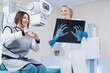 female doctor looks at an x-ray of hands and fingers in the radiology room against the background of medical equipment and happy patient. Comic shot of a patient laughing with a doctor. no wrist fract