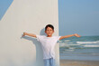 Portrait of smiling Asian boy open arms wide and looking at camera while standing on sailboat on the beach.