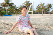 Smiling Asian young girl child relax on beach sand and looking camera at summer holiday.