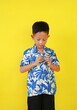 Portrait of Asian boy child buttoning up their own shirt isolated on yellow studio background.