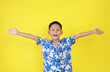 Portrait of happy Asian boy child in summer dress costumes raised arms or open hands wide gesture isolated on yellow background.