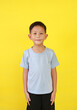 Portrait of smiling Asian boy age about 6 years old looking straight at camera isolated on yellow studio background.