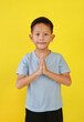 Portrait of Asian boy child age about 6 years old Pay respect or pray gesture isolated on yellow background.