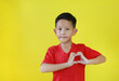 Portrait of happy Asian boy with a heart shape symbol with hands isolated on yellow background.