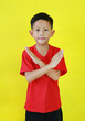 Asian boy child in red casual age 7 years old crossed his hands gesture isolated on yellow background. Happy child show stop sign or making X sign arms and looking camera.