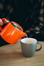 A Man Pours Tea From A Bright Orange Teapot Into A Cup.