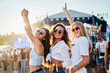 © artiemedvedev - Three joyful girls dance at sunny summer beach music festival, arms raised in celebration. Female friends enjoy live concert, fun times together surrounded by crowd, ocean backdrop during sunset.