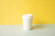 Disposable paper coffee cup on gray table. yellow wall background