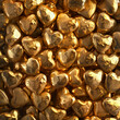 Fondo con detalle y textura de multitud de piezas de oro con forma de corazon, reflejos y brillos