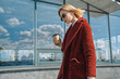 Beautiful caucasian woman walking along in the city. Stylish female model with sunglasses walking on city building terrace with cup of coffee. Window shopping concept