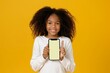 © MiraCle72 - Joyful african american girl demonstrating smartphone with blank screen and thumbs up on sunny yellow background