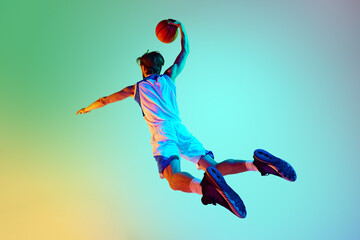 Competitive man, athlete in motion, training, playing basketball against gradient background in neon light. Concept of sport, competition, active and healthy lifestyle, game