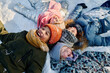 © pressmaster - Several intercultural kids in beanie hats and warm jackets lying on snow and laughing while enjoying winter vacation or weekend