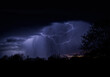 Cloud-to-air lightning illuminating a rain shaft pouring out of the storm cloud at night