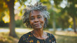 © Lucy - Portrait of a senior older black woman, natural looking smile to camera with out of focus park setting in background.