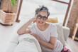 Photo of nice senior woman sit sofa have rest dressed white clothes cozy living room home house flat indoors pension concept