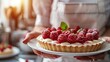 Joyful chef presents raspberry tart, warm kitchen backlight, eyelevel, soft focus