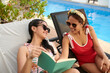 © DragonImages - Sunbathing mother and teenage daughter discussing book