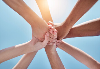 People, teamwork and hands together below for unity, collaboration or synergy on a blue sky background. Closeup or low angle of group or community in trust or solidarity for care, support or mission