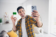 Photo of handsome cheerful guy dressed plaid shirt recording video modern gadget showing okey sign indoors room home house