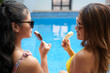 © DragonImages - Smiling mother and daughter in sunglasses eating icecreams and looking at each other