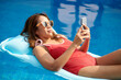 © DragonImages - Woman relaxing on inflatable matters and texting friends