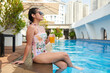 © DragonImages - Smiling teenage girl in swimsuit enjoying glass of fresh juice when sitting at pool