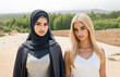 Two beautiful girls, one wearing islamic hijab clothes and the other a blonde western caucasian girl in blouse with bare neck and arms.