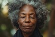 Grateful Senior African American woman closing eyes in Spiritual contemplation standing outside, close-up face of one black elderly gray hair lady in 80s feeling presence of GOD