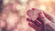 Hand holding heart-shaped object with blurred background. Bokeh photography with space for text. Love and care concept for greeting card, banner, poster