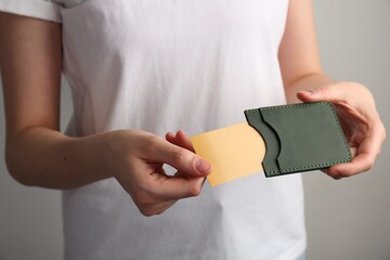 Wall Mural - Woman holding leather business card holder with card on grey background, closeup