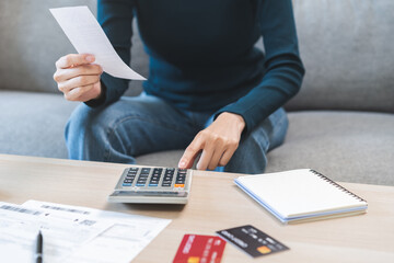 Wall Mural - Stressed asian young business woman, employee using calculator to calculate expenses of monthly, hand holding bills and receipt for to payment on table at home. Financial, finance of banking concept.