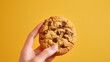 Hand holding a gourmet cookie, deep yellow solid pastel background, minimalistic closeup ad,