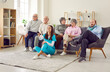 Group of happy diverse senior people sitting on sofa together watching TV in retirement home with a young female friendly nurse holding remote. Leisure in nursing home and caregiver support concept.