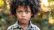 African American youngster with curly hair dressed casually looks solemn and unconstrained gazing directly at the camera
